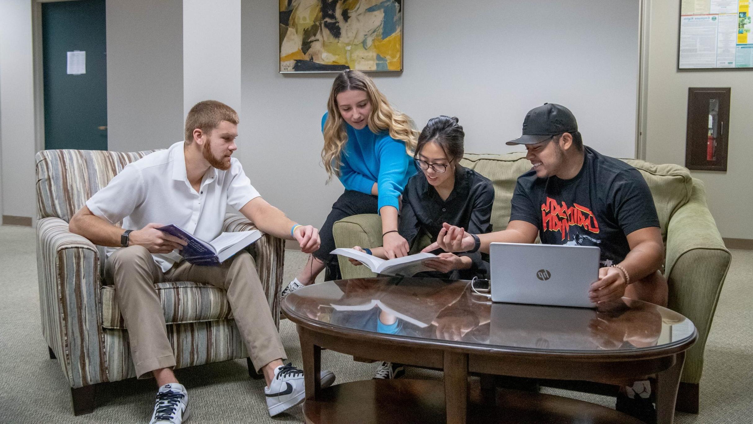 Students gathered around a table in a sitting area with a book and laptop.